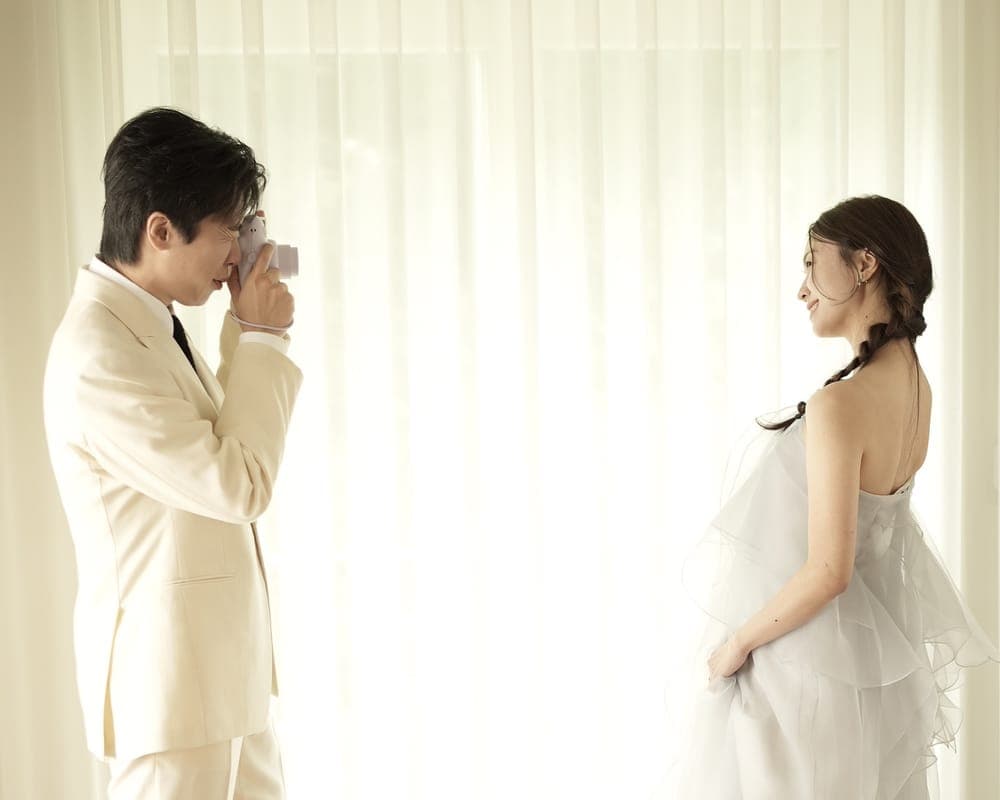 신랑이 즉석카메라로 창가에 선 신부를 찍는 모습